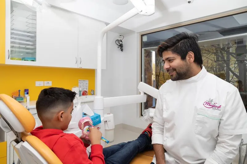 A Magical Smiles dentist showing a child how to brush using a teeth model and toothbrush.