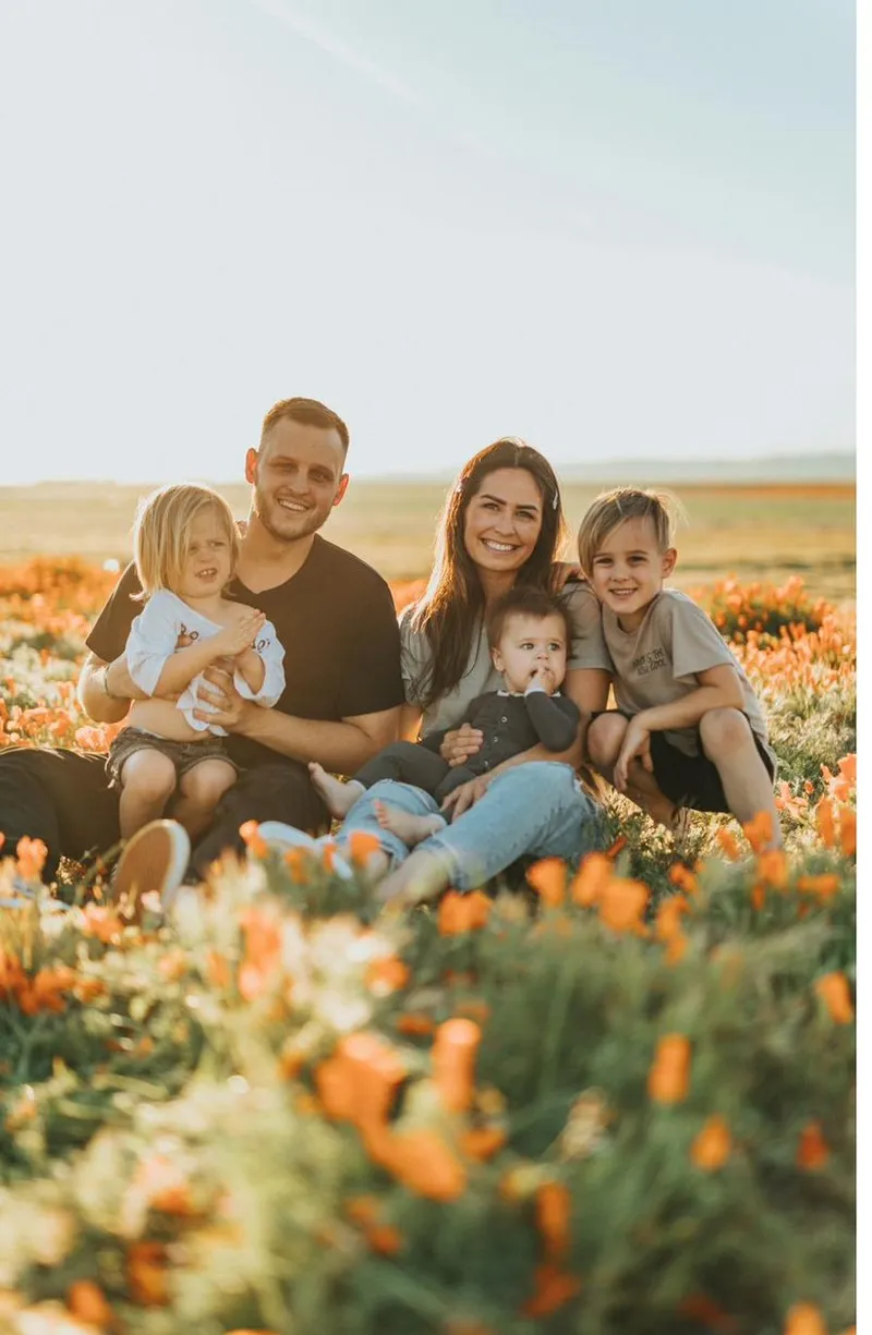 A warm family of five sitting together outdoors in soft golden light.