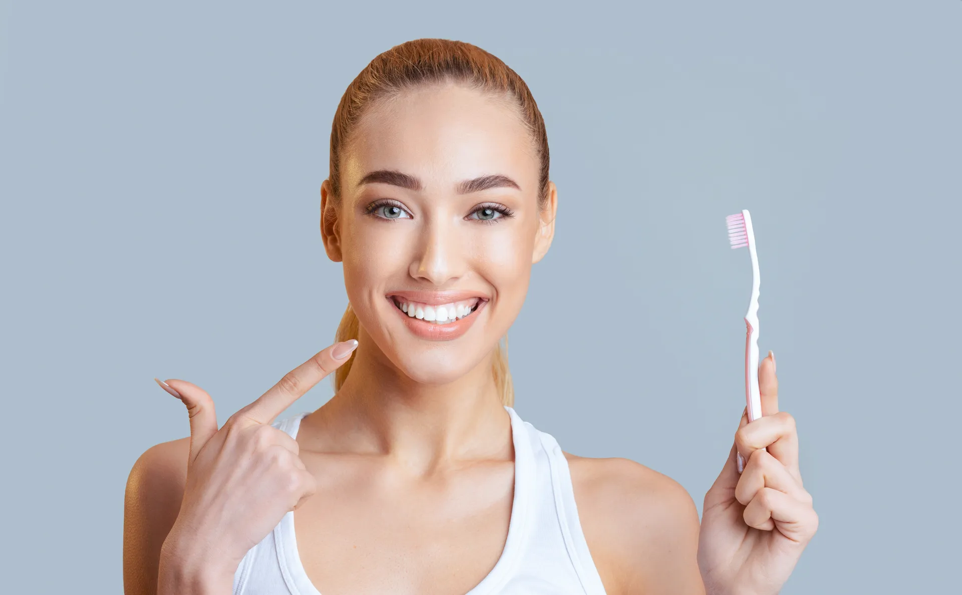 A woman pointing to her teeth while holding a toothbrush, talking about her cleaning routine