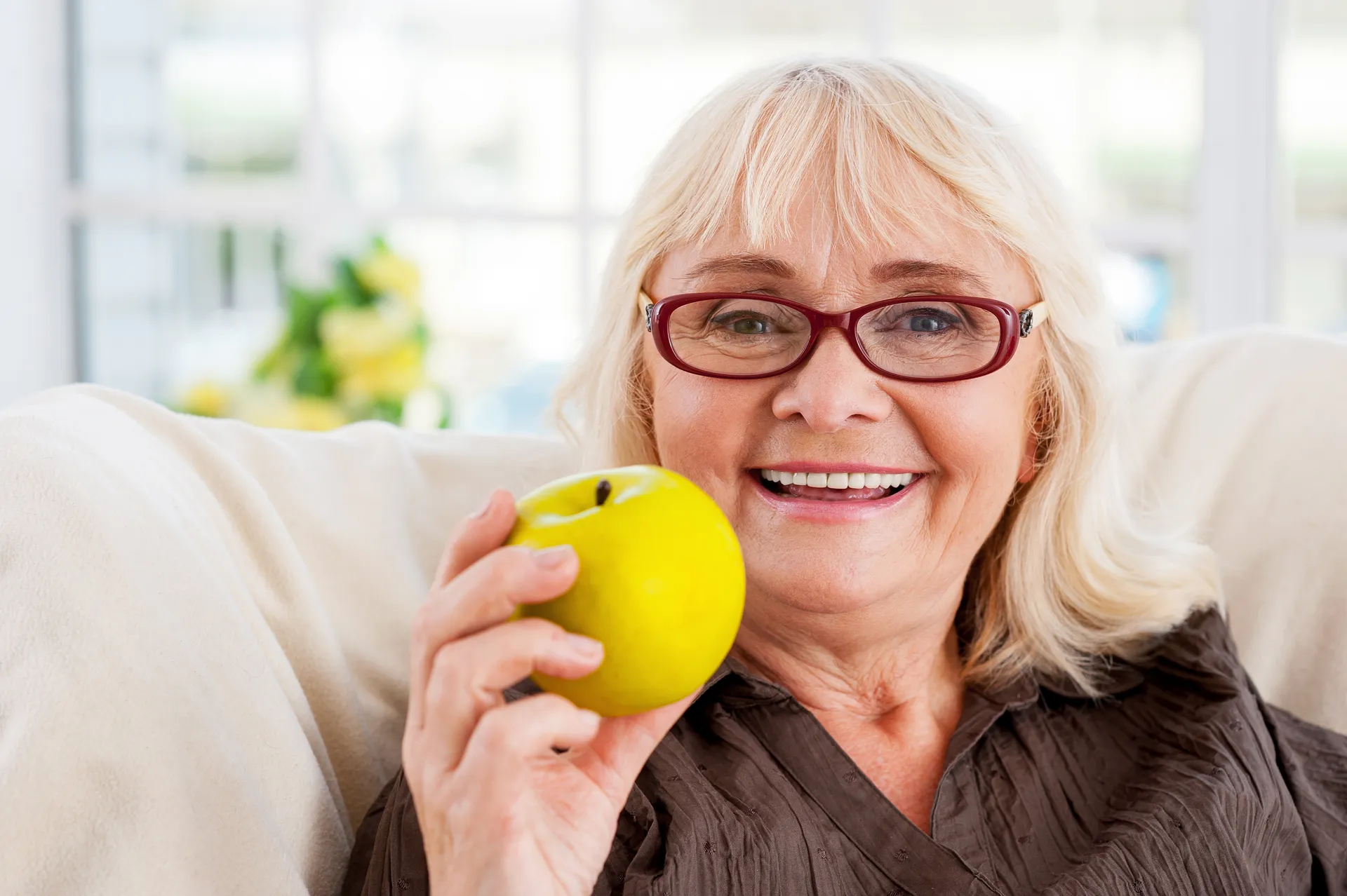 A smiling senior woman holding an apple, enjoying everyday food