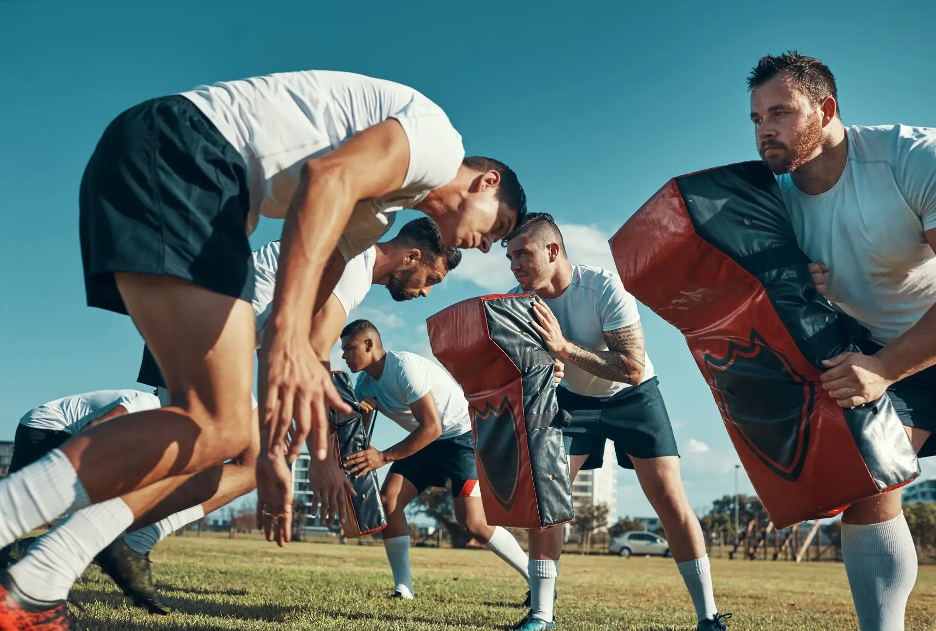 Rugby players training with tackle pads on a sunny outdoor field