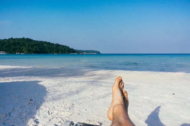 Person lying back on the sand with their feet towards the sea, evoking the calm of a gentler injection