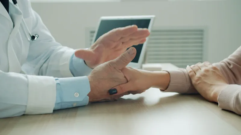 A clinician speaking calmly with a patient, a reassuring hand resting on their arm as they talk through what to expect