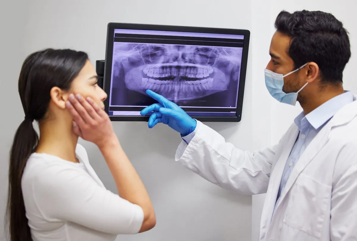 A dentist pointing out the wisdom teeth on a patient's panoramic X-ray