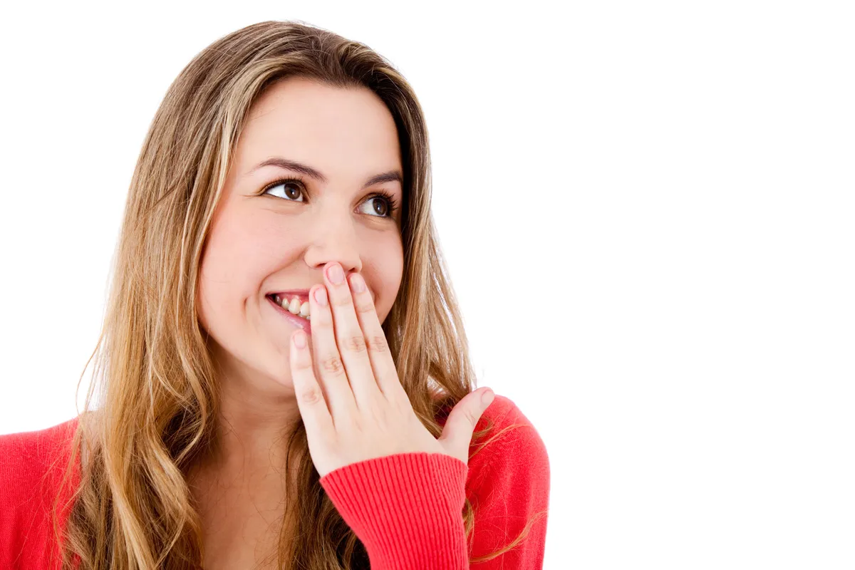 A woman laughing with her hand raised near her mouth, a common habit for people who feel self-conscious about their gum-to-tooth ratio